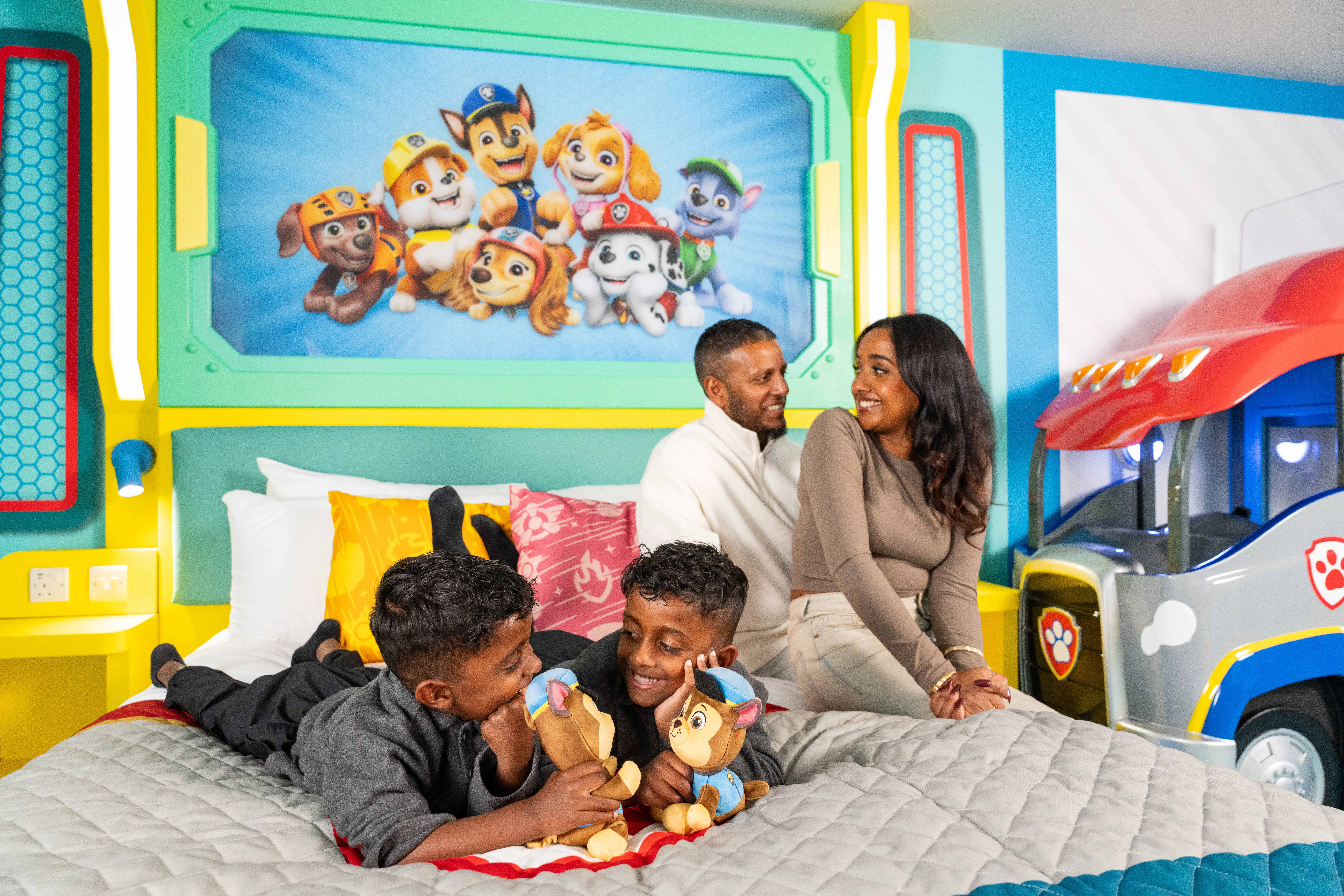 Mum, Dad and 2 children sat on bed in a PAW Patrol themed hotel room in the Chessington Safari Hotel